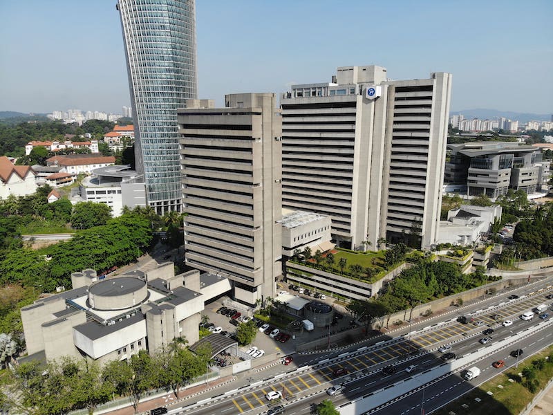 A large institutional building beside city roads and trees